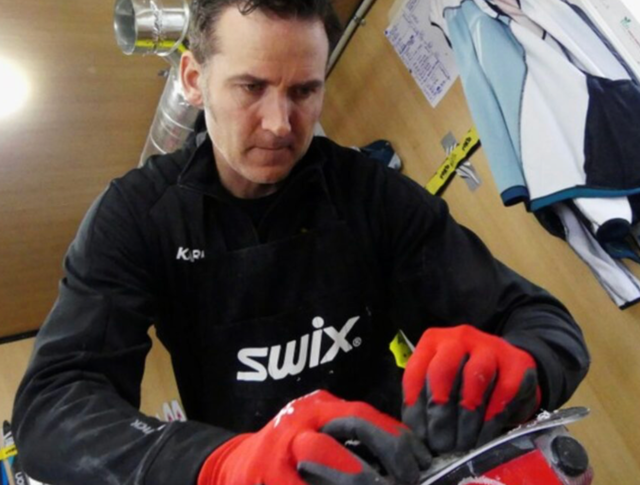 Randy Gibbs in a black Swix apron and red gloves works on a ski at an outdoor race venue