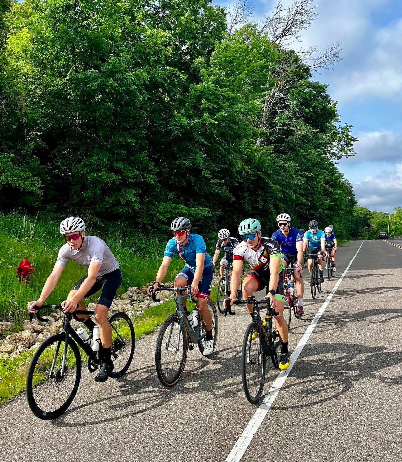 College athletes on a group road ride through green summer woods