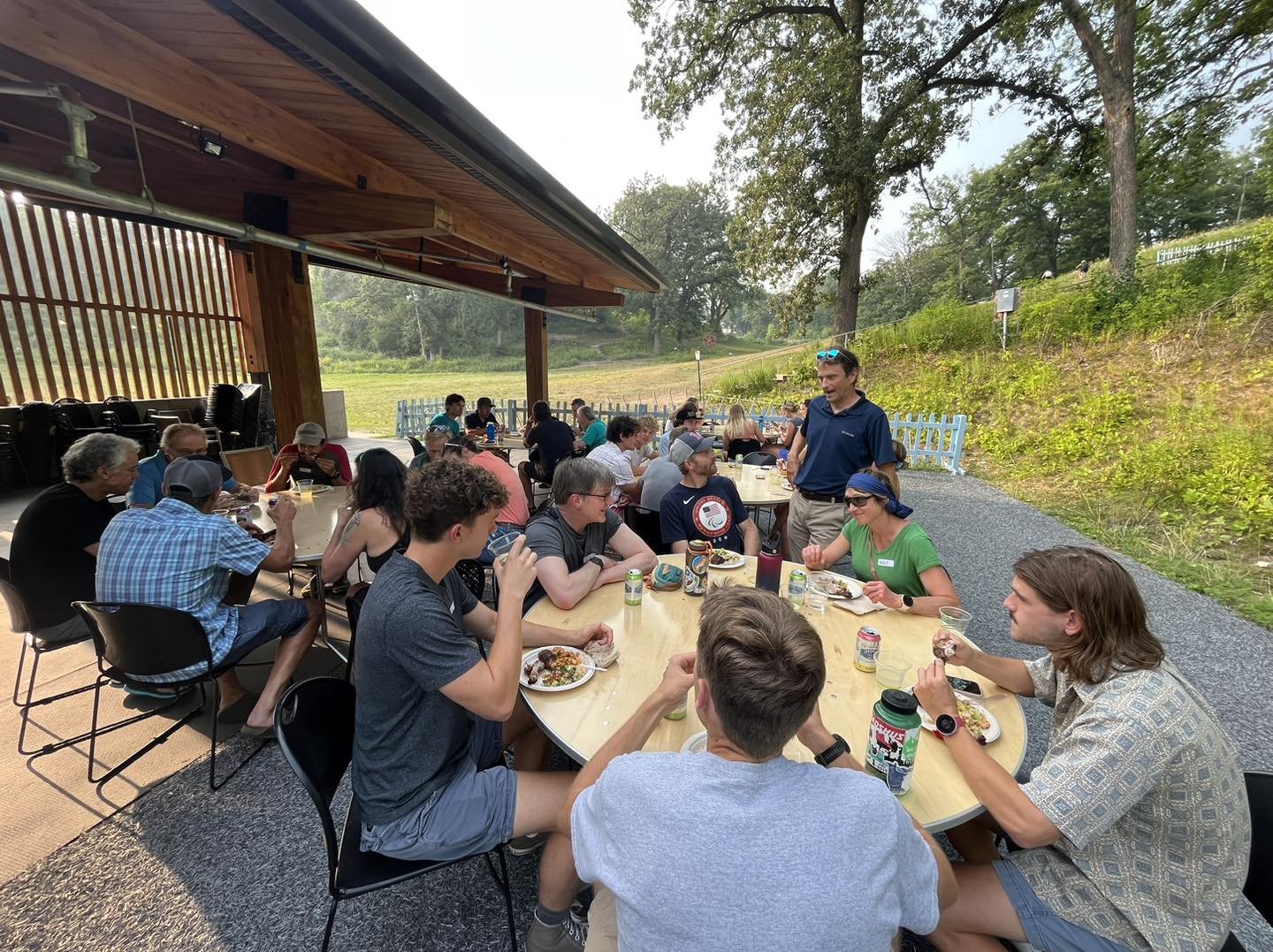 Team supporters gathered for a meal at a covered pavilion among trees